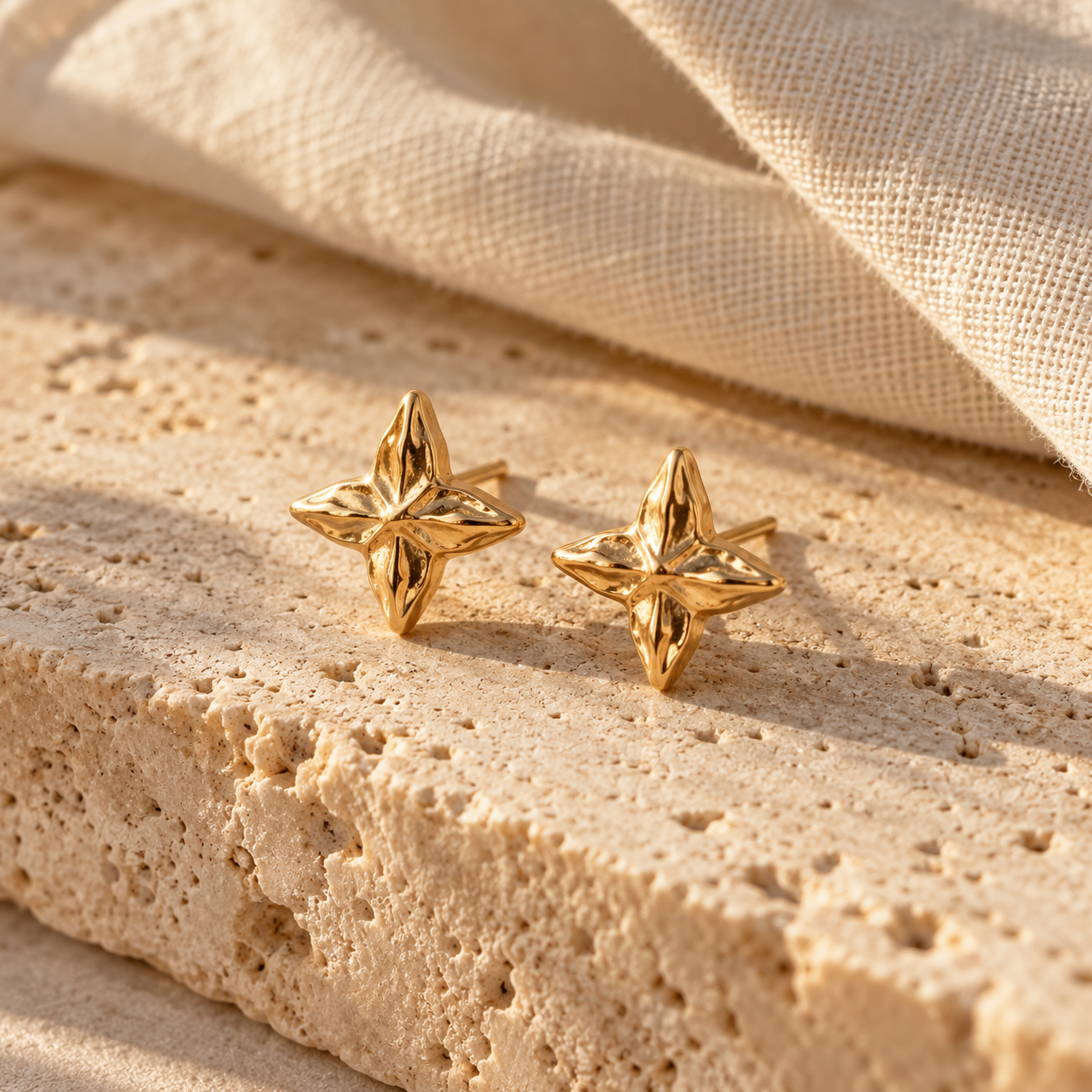 Small four-pointed Malaika gold star stud earrings on ivory linen